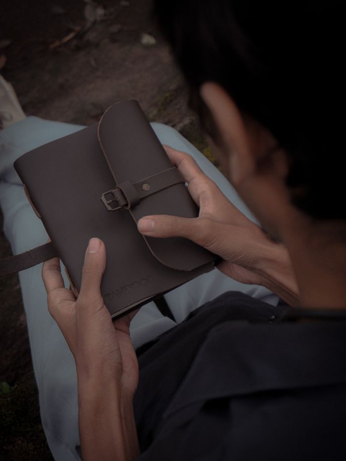 services-01 Unrecognizable person sitting outdoors holding a brown leather diary in their hands.