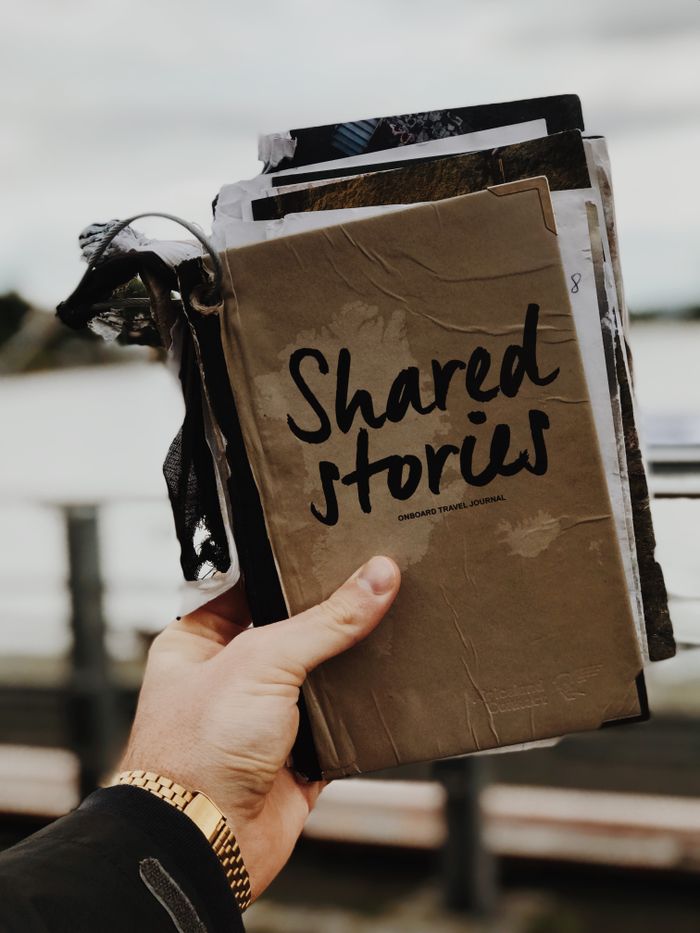 services-02 Hand holds a "Shared Stories" journal against a blurred outdoor backdrop, emphasizing creativity and personal storytelling.