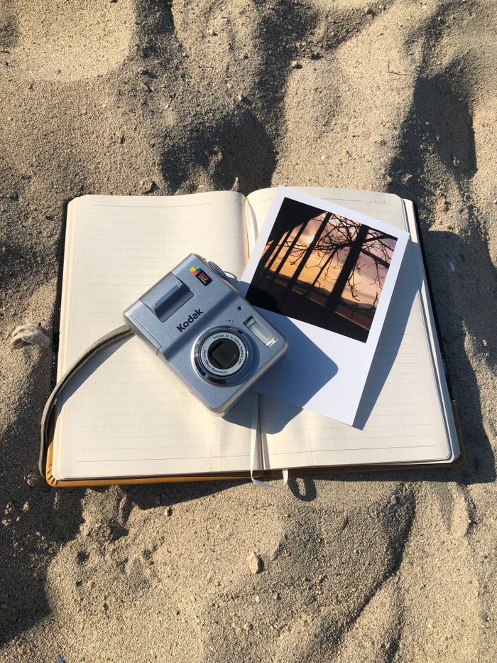 about-us-02 A vintage camera, photo, and open notebook on sandy ground, capturing nostalgia.