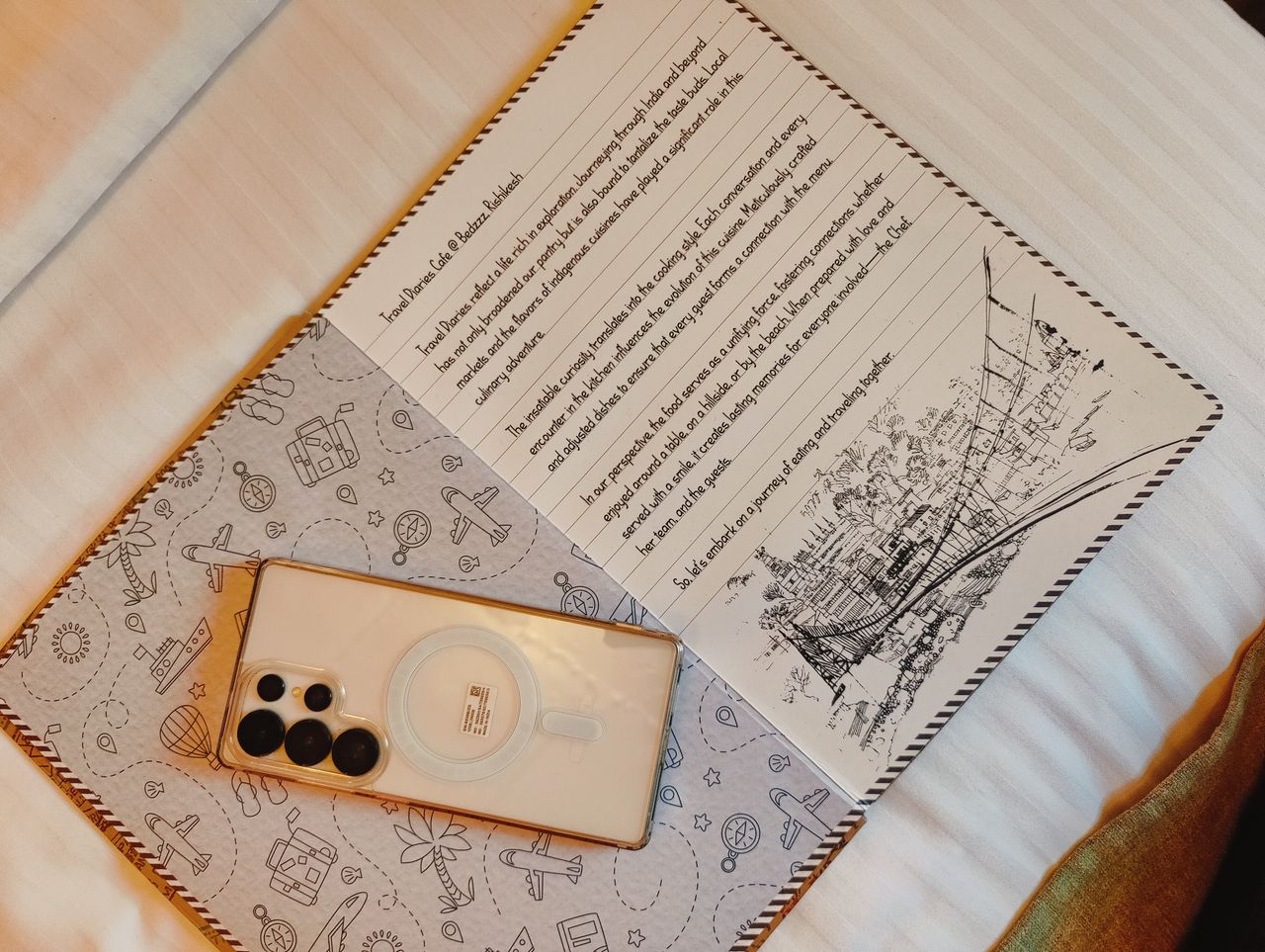 Open notebook with handwritten text next to a smartphone on a bed, cozy indoor setting.