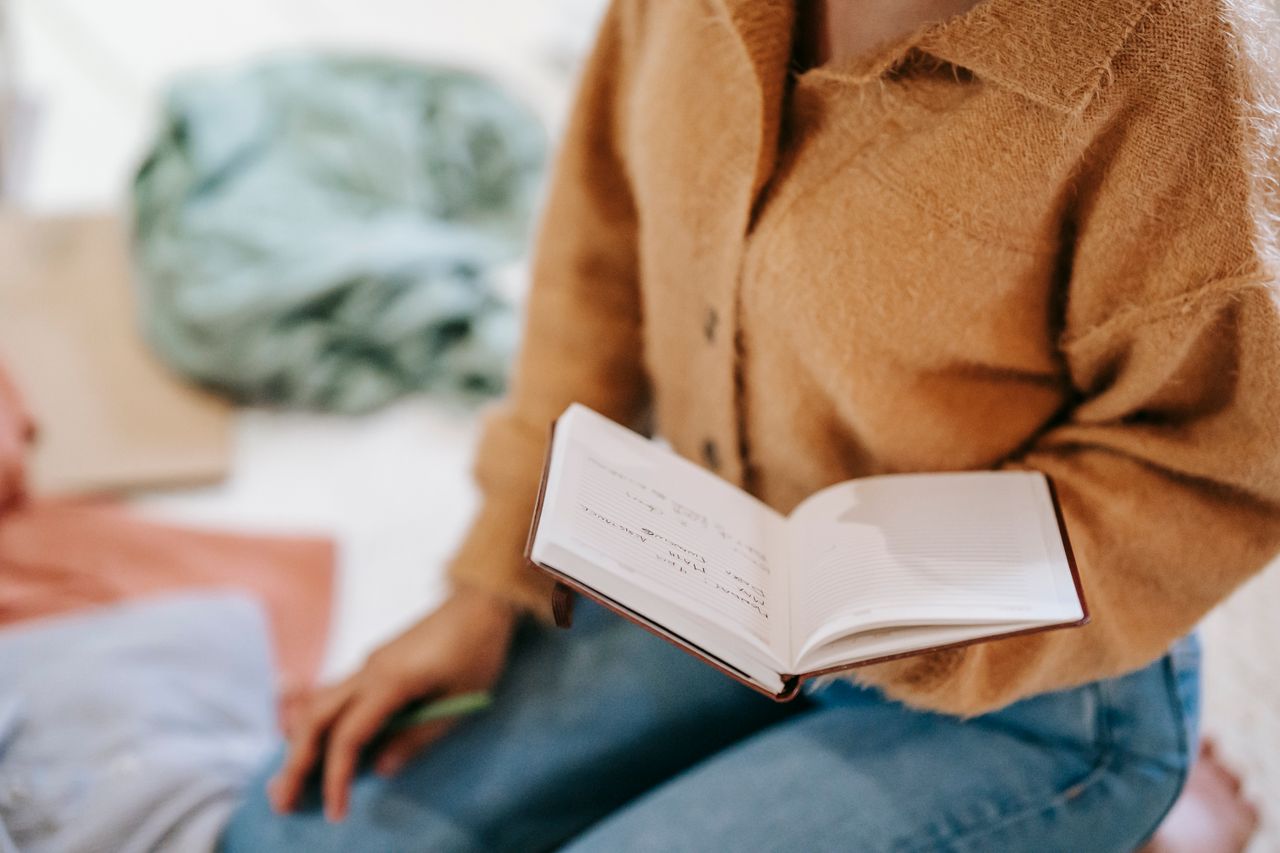 services-03 Crop anonymous female in casual clothes reading notes in notebook while sitting on floor in light room